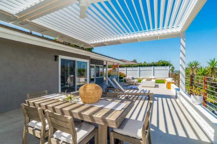 An inviting outdoor dining space with a wooden table, cushioned chairs, and a stylish lattice shade providing natural light and shade.