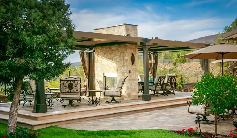 A tranquil patio setup featuring comfortable seating, a cozy fireplace, and lush greenery, perfect for relaxation.