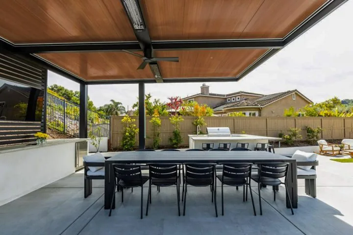 A modern patio cover featuring a dining table, comfortable chairs, and a ceiling fan, creating a relaxing outdoor space.